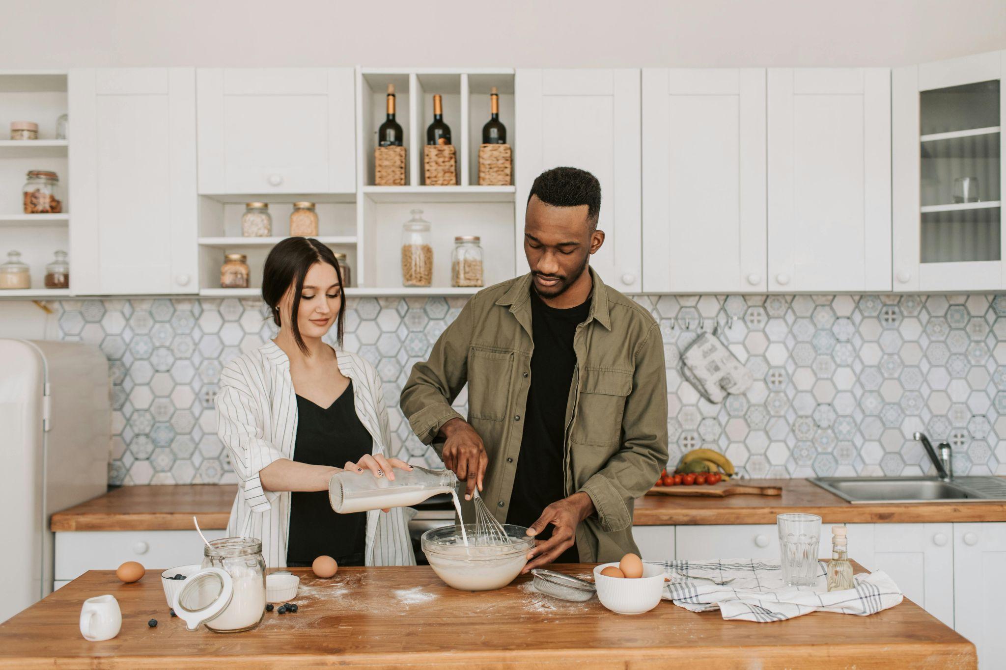 A Couple cooking together in a kitchen with a hexagon tile backsplash.